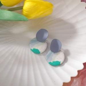 Abstract geometric clay earrings in mint green and grey-blue on a white shell tray