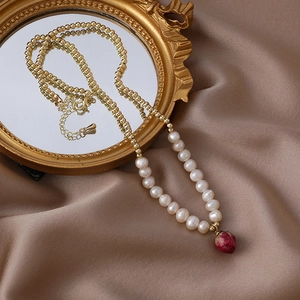 Detail of pearl necklace with red dried rose pendant on vintage brown silk fabric