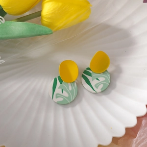 Detail of clay drop earrings featuring yellow studs and green monstera leaf patterns