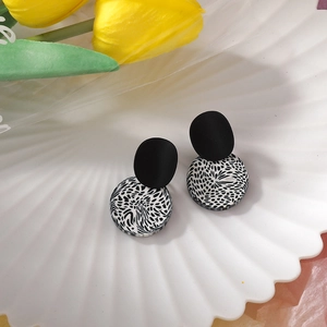 Macro view of geometric clay earrings with black matte studs and monochrome patterns