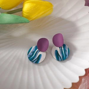 Detail of handmade geometric earrings with purple semi-circle and blue-green marbled disc