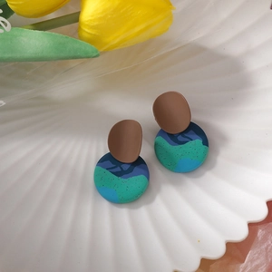 Close-up of geometric handmade clay earrings with blue and green abstract patterns