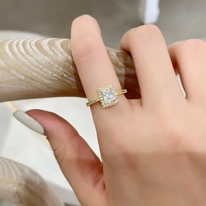 Gros plan d'une bague dorée avec un zircon rectangulaire serti en halo sur un doigt