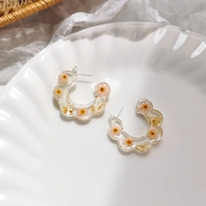 Detailed close-up of resin C-shape earrings with dried flowers and gold foil elements