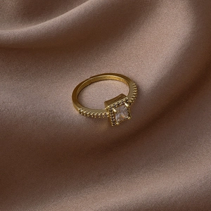 Détail macro d'une bague dorée avec zircon carré et pavage sur fond de soie marron
