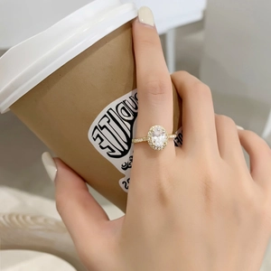 Gros plan d'une bague dorée ornée d'un grand zircon ovale avec sertissage halo sur le doigt