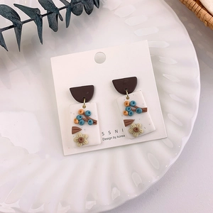Macro shot of handmade floral earrings with 3D yellow flowers on a white base detail