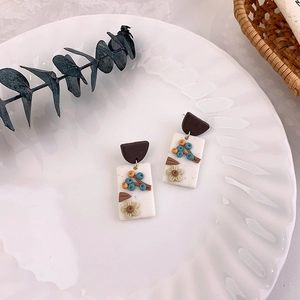 Detailed macro view of handmade floral clay earrings on a decorative white ceramic plate