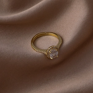 Détail macro d'une bague ajustable dorée avec halo de zircone cubique sur fond de soie