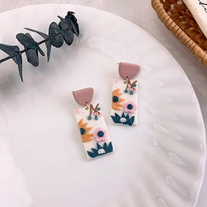 Detail of floral clay earrings featuring pink blossoms and blue leaves on white ceramic