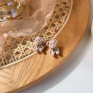 Close-up of brown flocked bear earrings with black bowknot detail on a rustic wooden tray