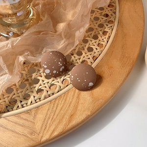 Close-up of vintage brown matte round stud earrings with artistic white ink splatter texture