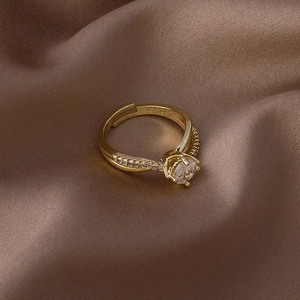 Détail d'une bague dorée avec zircon rond et anneau torsadé croisé sur du satin