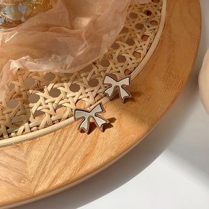 Close-up of retro bow earrings with beige and brown enamel on a textured background