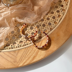 Close-up of vintage brown checkered resin C-hoop earrings on a woven tray