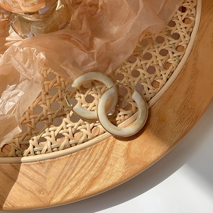 Close-up of vintage beige marble resin hoop earrings with gold trim on rattan tray