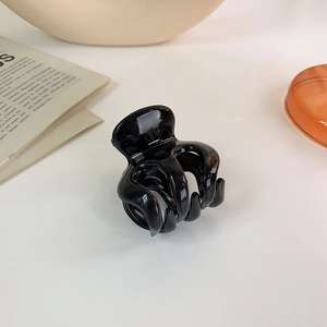 Close-up of small glossy black hair claw clip for high ponytail on white surface