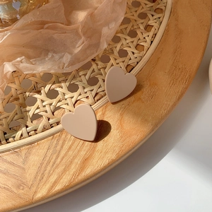 Close-up of matte cream heart-shaped earrings on a textured rattan tray