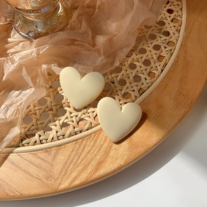Detail of cream white heart earrings set on a textured wooden tray with warm lighting