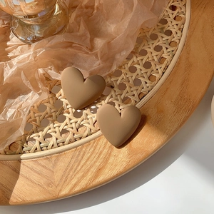 Macro shot of matte heart-shaped earrings in earthy taupe on a woven rattan texture