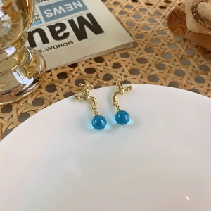 Close-up of golden faucet stud earrings with blue crystal balls on a white plate