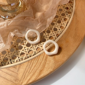 Artistic cream-colored irregular matte round earrings on a rustic woven tray setup