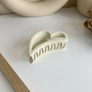 Pince à cheveux cœur évidé crème mate sur un socle minimaliste et lumière douce