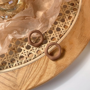Close-up of brown matte resin earrings with wavy irregular shapes on a woven tray