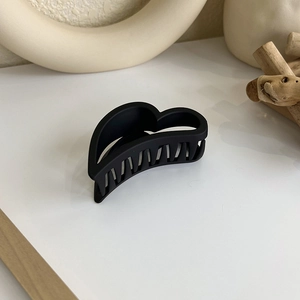 Gros plan d'une pince à cheveux noire mate en forme de cœur sur une surface blanche