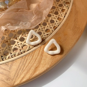 Detailed view of cream white triangle stud earrings on a rustic woven tray