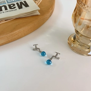 Detail of silver faucet stud earrings with a clear blue water drop bead on a rustic background