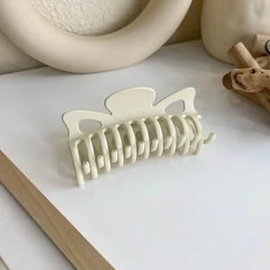 Détail d'une pince à cheveux mate crème avec design ondulé et dents solides
