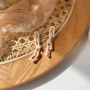 Detailed close-up of cream matte chain link earrings placed on a woven rattan tray