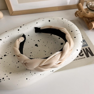 Détail d'un serre-tête tressé en satin champagne sur un plateau décoratif de style rétro