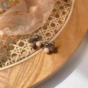 Detail view of retro bow-knot earrings with matte cream and brown beads on a woven tray