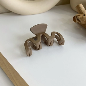 Détail d'une pince à cheveux mate marron café au design ondulé sur surface blanche