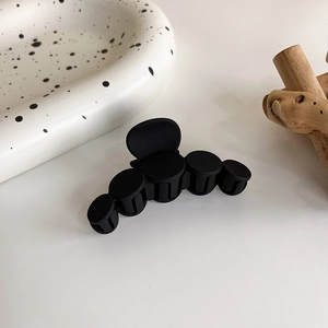 Détail d'une grande pince à cheveux noire mate avec design modulaire circulaire sur bois