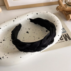 Détail d'un serre-tête tressé en satin noir au lustre soyeux sur plateau céramique