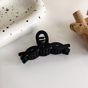 Détail d'une grande pince à cheveux noire mate au design torsadé moderne sur plateau