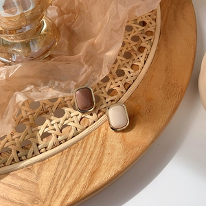 Close-up of minimalist rectangular earrings in brown and cream on a wooden tray