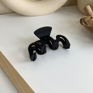 Détail de la pince à cheveux noire mate ondulée sur fond décoratif minimaliste épuré