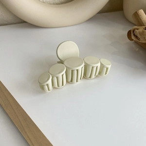 Gros plan d'une pince à cheveux mate blanc crème au design cylindrique minimaliste