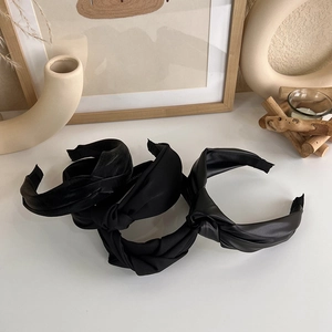 Detailed view of three black knotted headbands in leather, satin and fabric textures