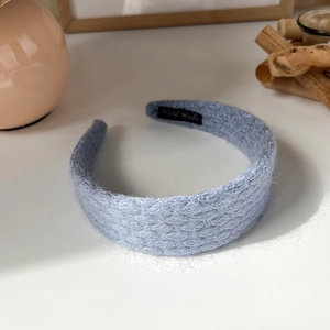 Detailed view of light blue knitted headband with handmade label on white desk