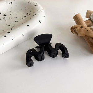 Détail d'une grande pince à cheveux noire mate au design ondulé sur fond minimaliste