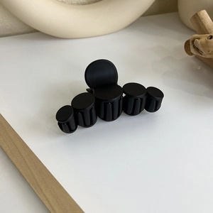 Gros plan d'une pince à cheveux noire mate avec cinq dents sur une surface blanche