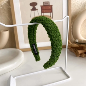 Detail of green tweed woven headband featuring a black handmade label on the side