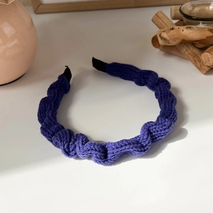 Detail of a purple pleated knit headband with textured wavy fabric on a white surface