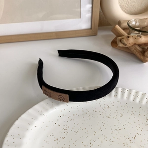 Close-up of black fabric headband featuring a brown leather Hand Made label and smiley icon