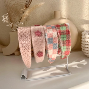 Pink plush headband set with floral and plaid knit patterns on a white metal stand